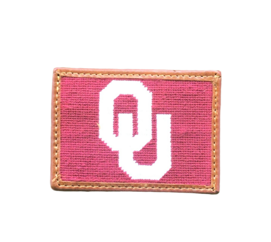 A pink needlepoint card wallet with a white "OU" logo and brown leather trim.