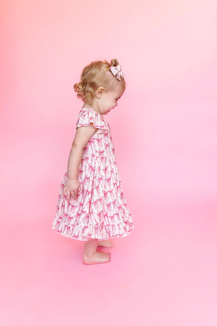 A toddler in a white and pink bow-patterned ruffle dress looks down.