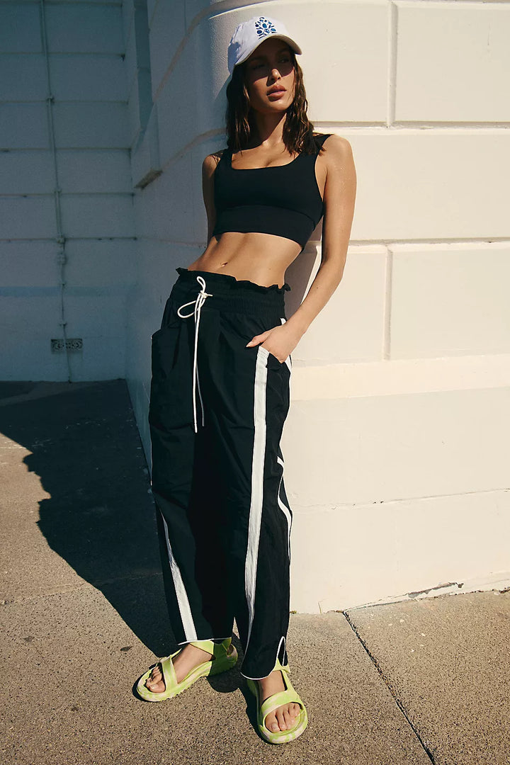 Black track pants with white side stripes and a ruffled elastic waistband.