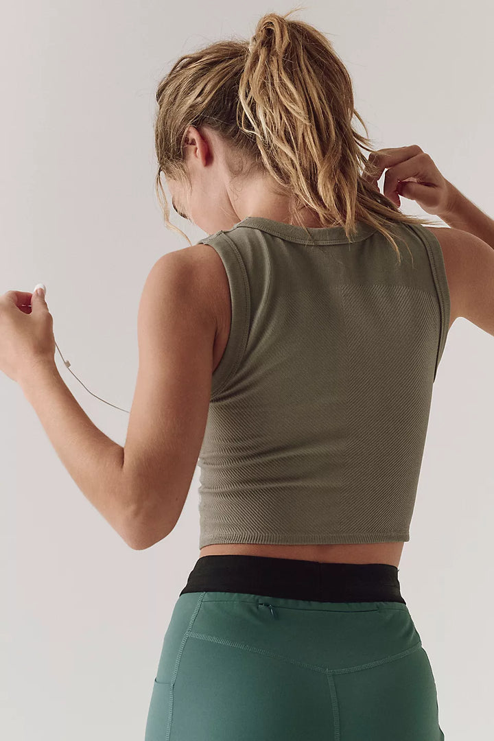 A woman from behind wears a sage green ribbed muscle tank and teal leggings.