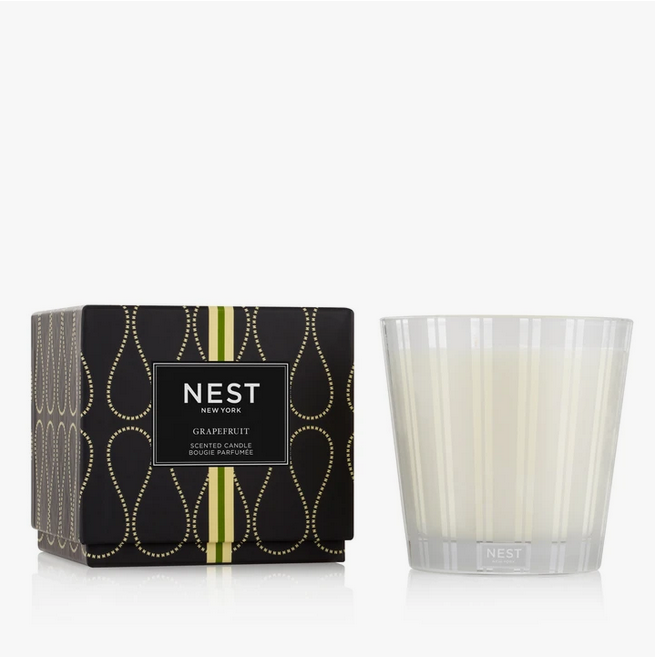 A Nest New York Grapefruit 3-Wick Candle in a clear glass holder next to its black box.