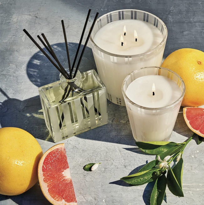 A grapefruit-scented 3-wick candle, a single-wick candle, and a reed diffuser are displayed with fresh grapefruits and citrus leaves.