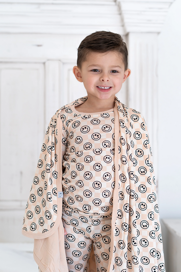A young boy smiles, wearing a Sandy Smiles Checker Dream Set with a matching robe.