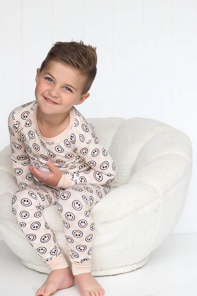A young boy in a Sandy Smiles Checker Dream Set sits on a white fluffy chair.