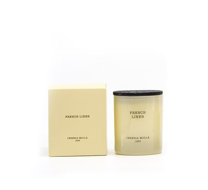 An ivory candle in a glass jar with a black lid, next to its matching box.