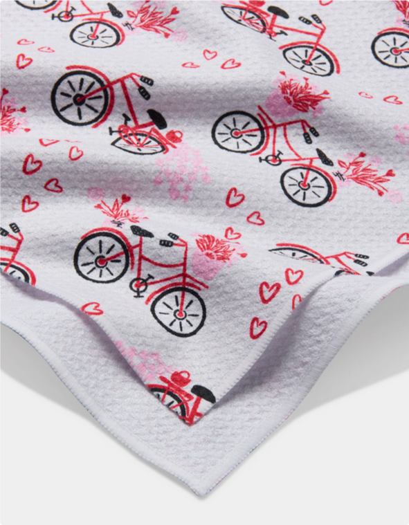 White tea towel with a pattern of red bicycles and hearts.
