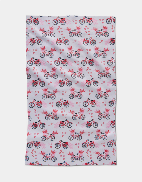 A white tea towel with a repeating pattern of red bicycles and pink hearts.