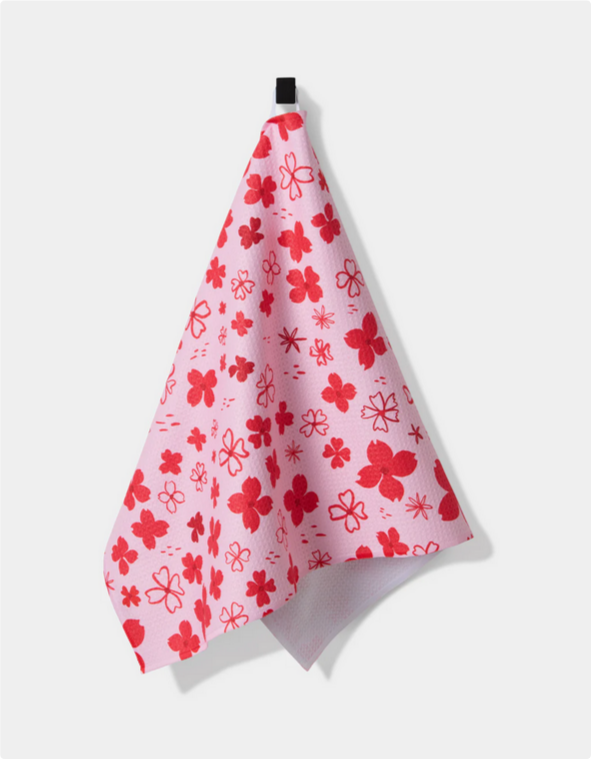 A pink tea towel with a red dogwood hearts pattern hangs from a black hook.