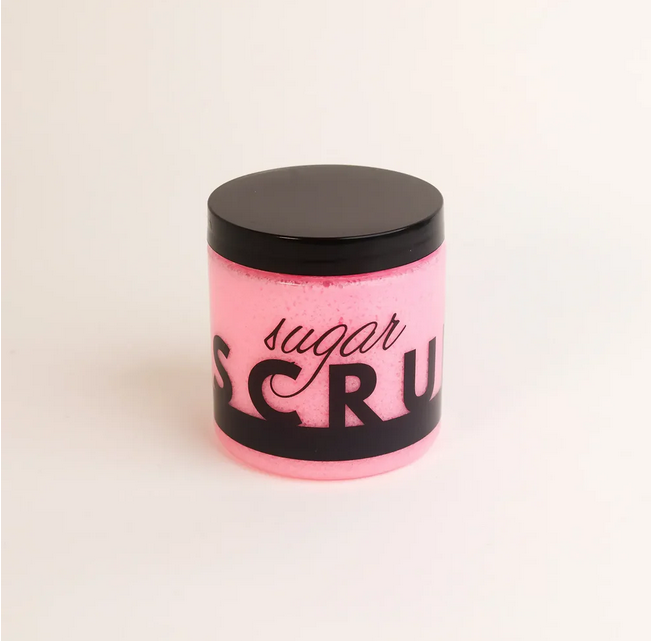 A pink sugar scrub in a clear jar with a black lid and "sugar SCRUB" label.