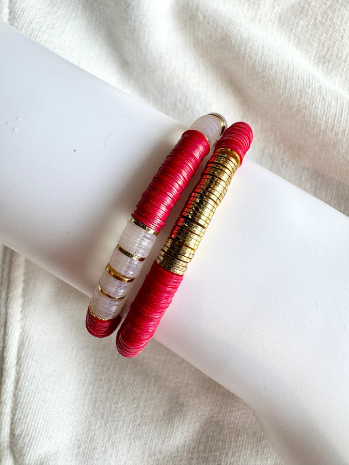 Two flat bead bracelets, one red and gold, the other white and gold, on a white surface.