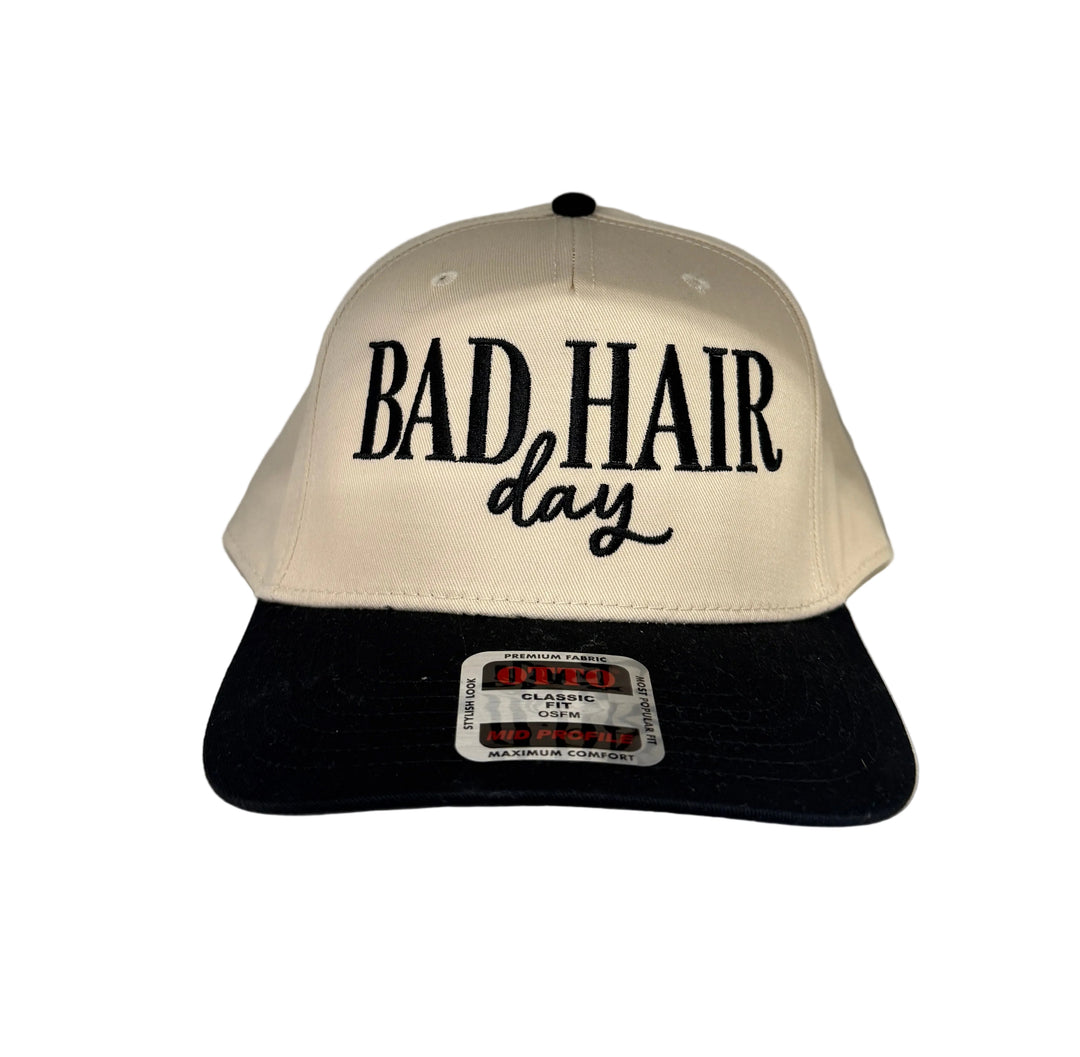 A beige and black baseball cap with "BAD HAIR day" embroidered on the front.
