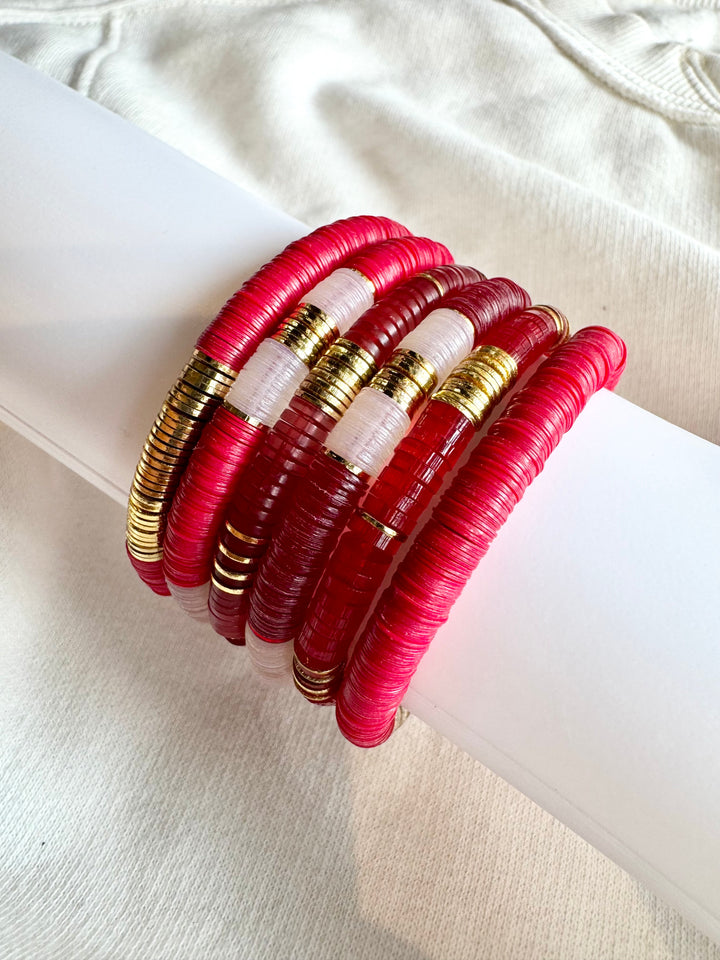 A stack of red, white, and gold flat bead bracelets.