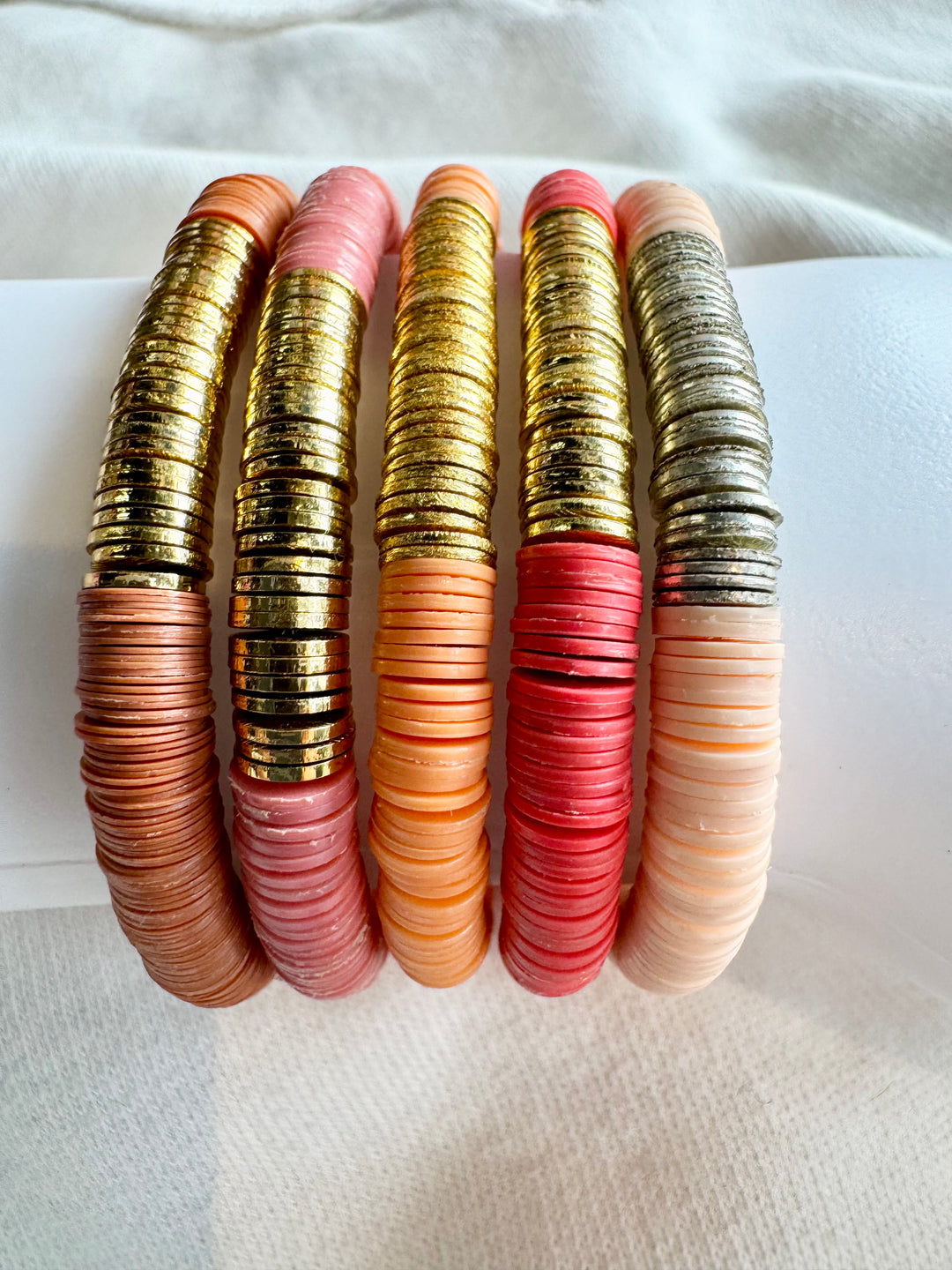 Five flat bead bracelets in shades of pink, orange, and red, with gold and silver accents.