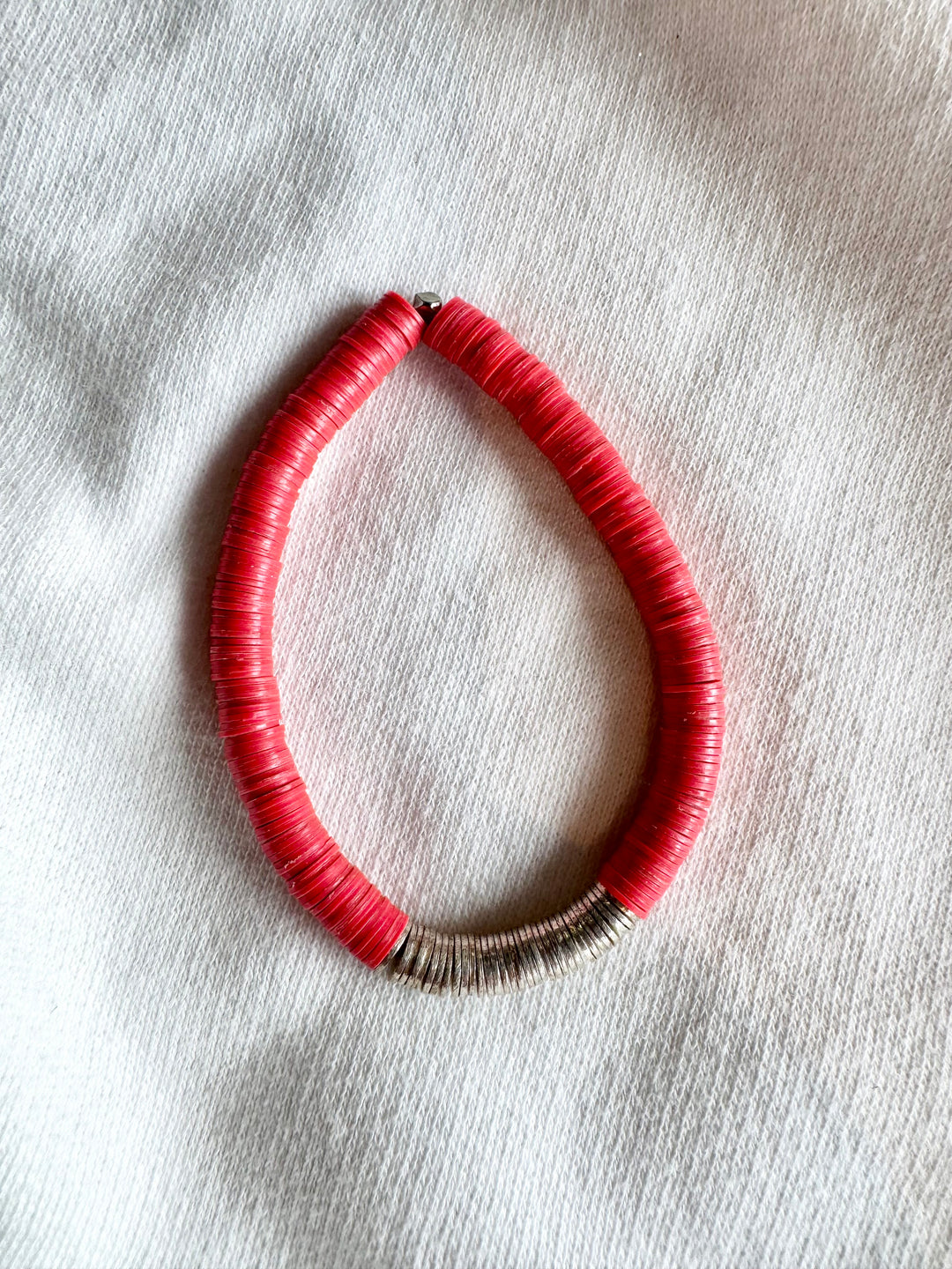 Large flat bead bracelet with red and silver beads on a white fabric background.