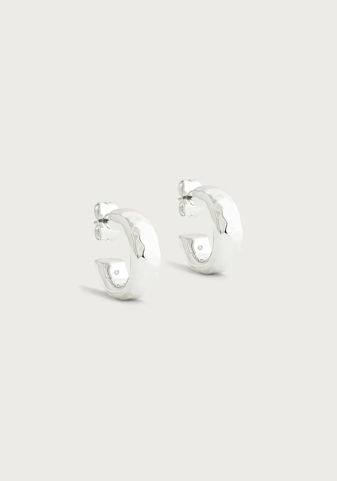 Silver huggie hoop earrings with a hammered texture and a small diamond accent.