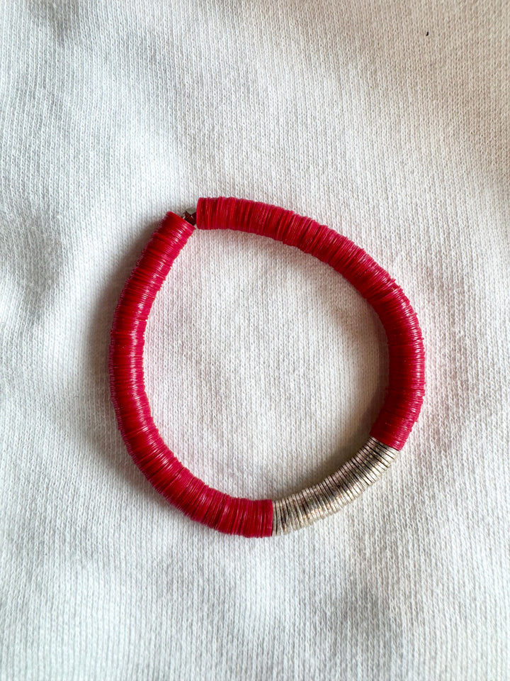 A red and silver flat bead bracelet is displayed on a white ribbed fabric.