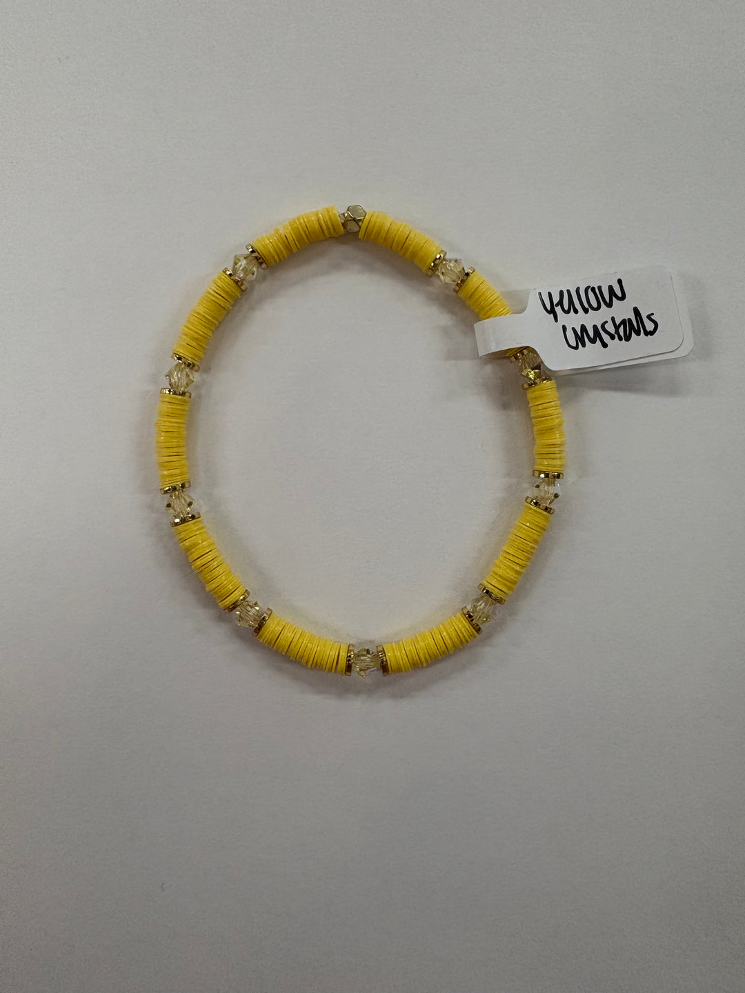 A yellow flat bead bracelet with clear crystal accents and a tag reading "Yellow Crystals."