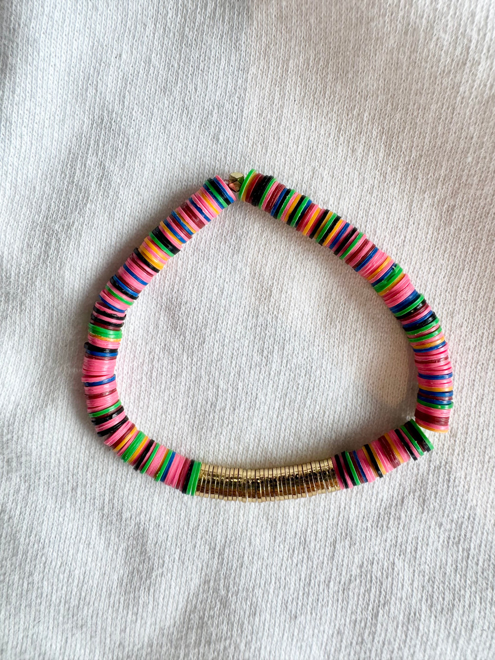 A colorful flat bead bracelet with a gold-plated section, arranged in a triangle shape.