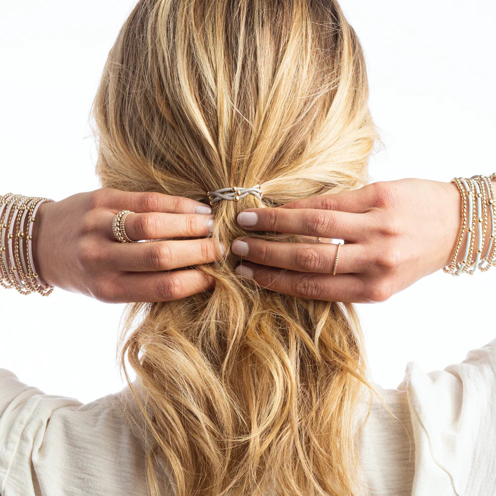 A blonde woman wears a neutral hair tie and matching beaded bracelets and rings.