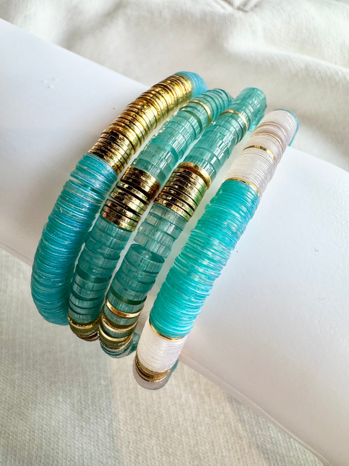 Four flat bead bracelets in shades of blue and white with gold accents.