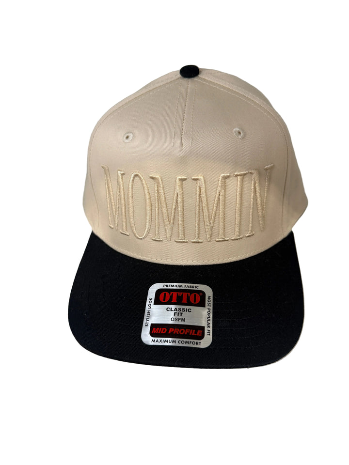 A cream canvas baseball cap with "MOMMIN" embroidered in cream and a black brim.
