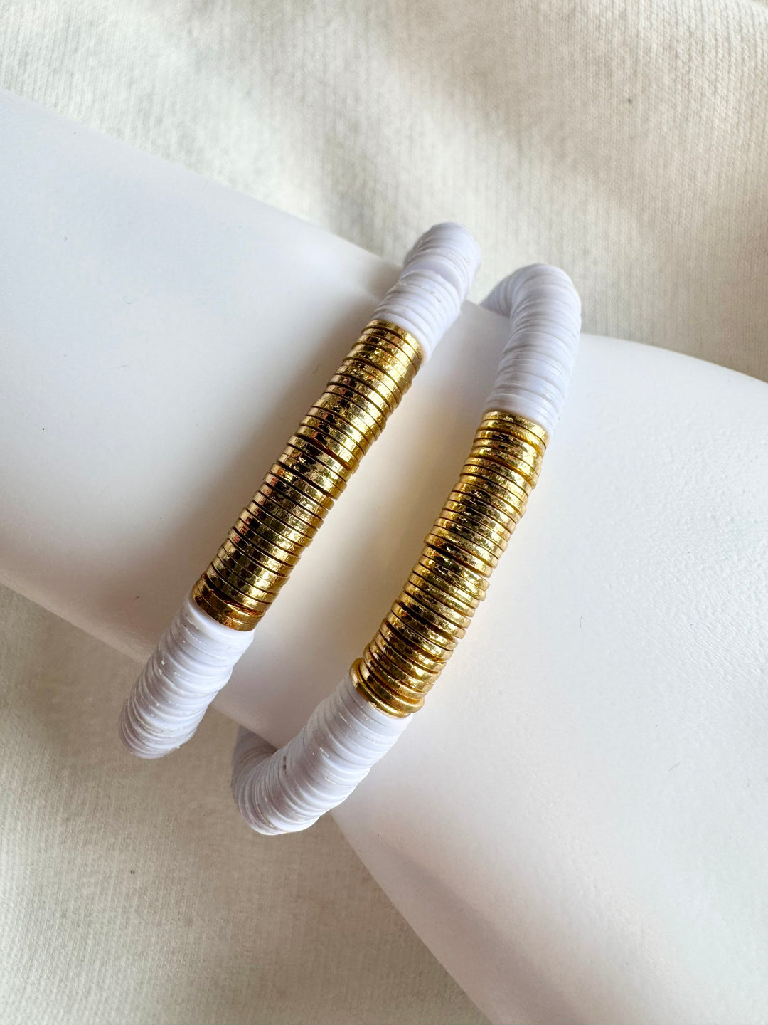 Two white flat bead bracelets with hammered gold-plated accents are displayed on a white surface.