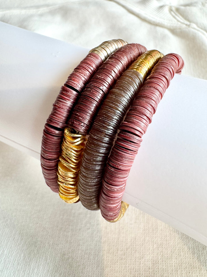 Four flat bead bracelets in shades of gold, silver, and maroon are stacked together.