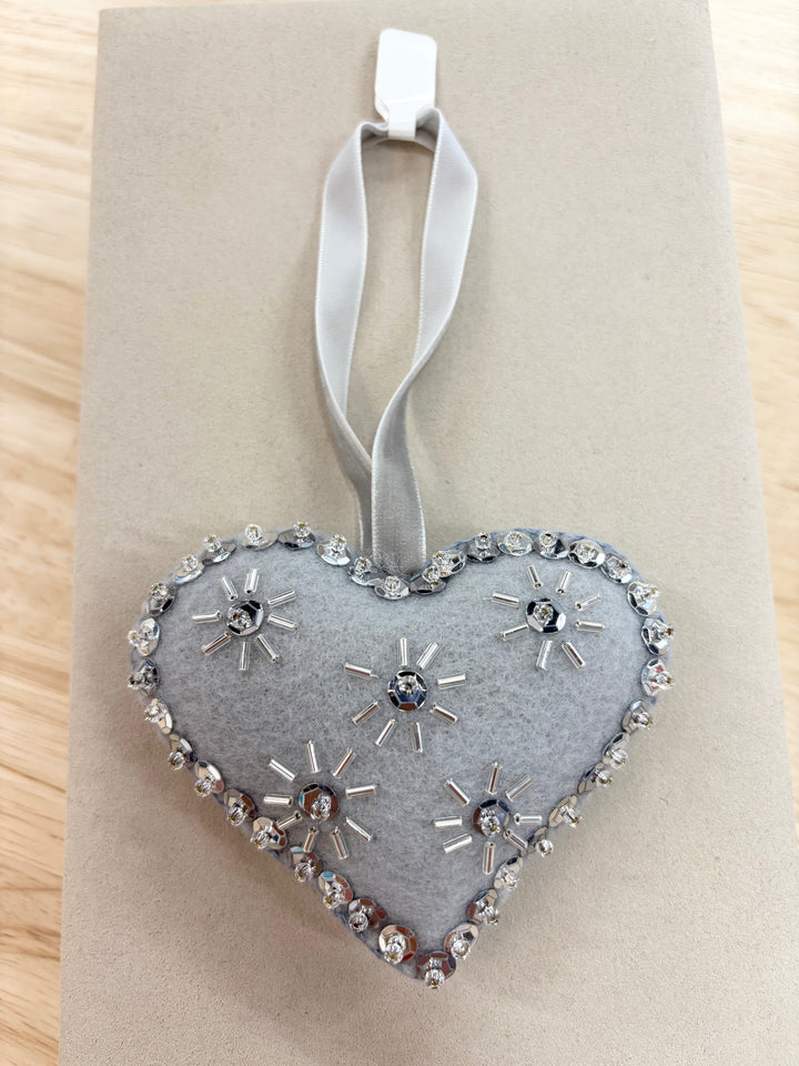 Heart-shaped, light gray felt ornament with silver beads and sequins, hanging from a white ribbon.