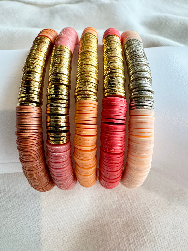 Five flat bead bracelets in shades of pink, orange, and gold.