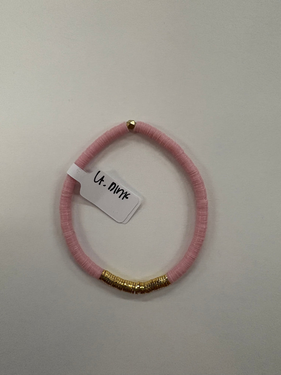 A light pink flat bead bracelet with a section of gold beads and a small gold bead at the top.
