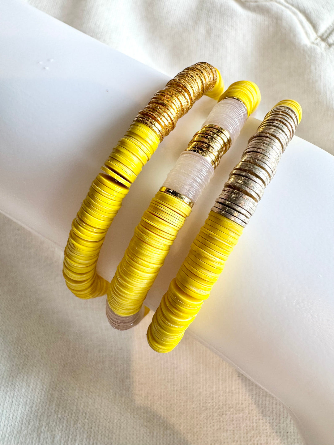 Three yellow flat bead bracelets, two with gold and one with silver accents.