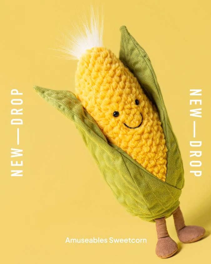 A plush toy corn cob with a smiling face and green husks.