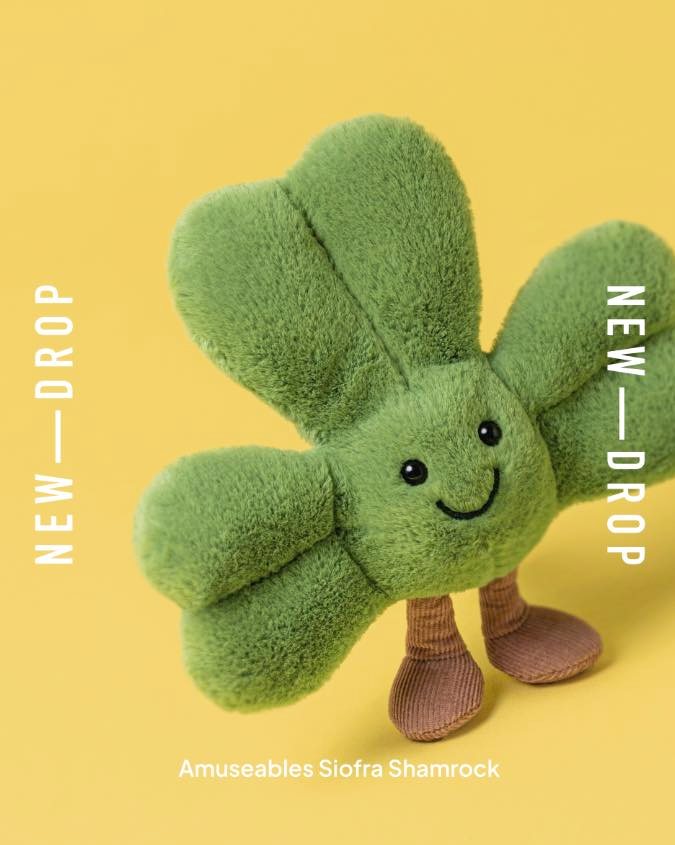 A green plush shamrock toy with a smiling face and brown feet.