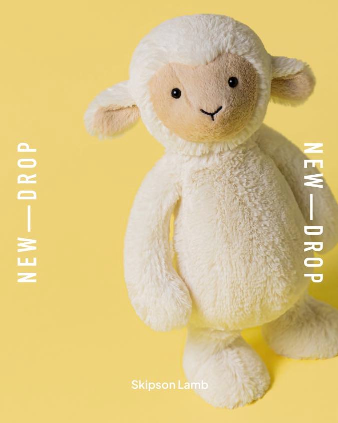 A fluffy white lamb stuffed animal with a tan face and ears sits against a yellow background.