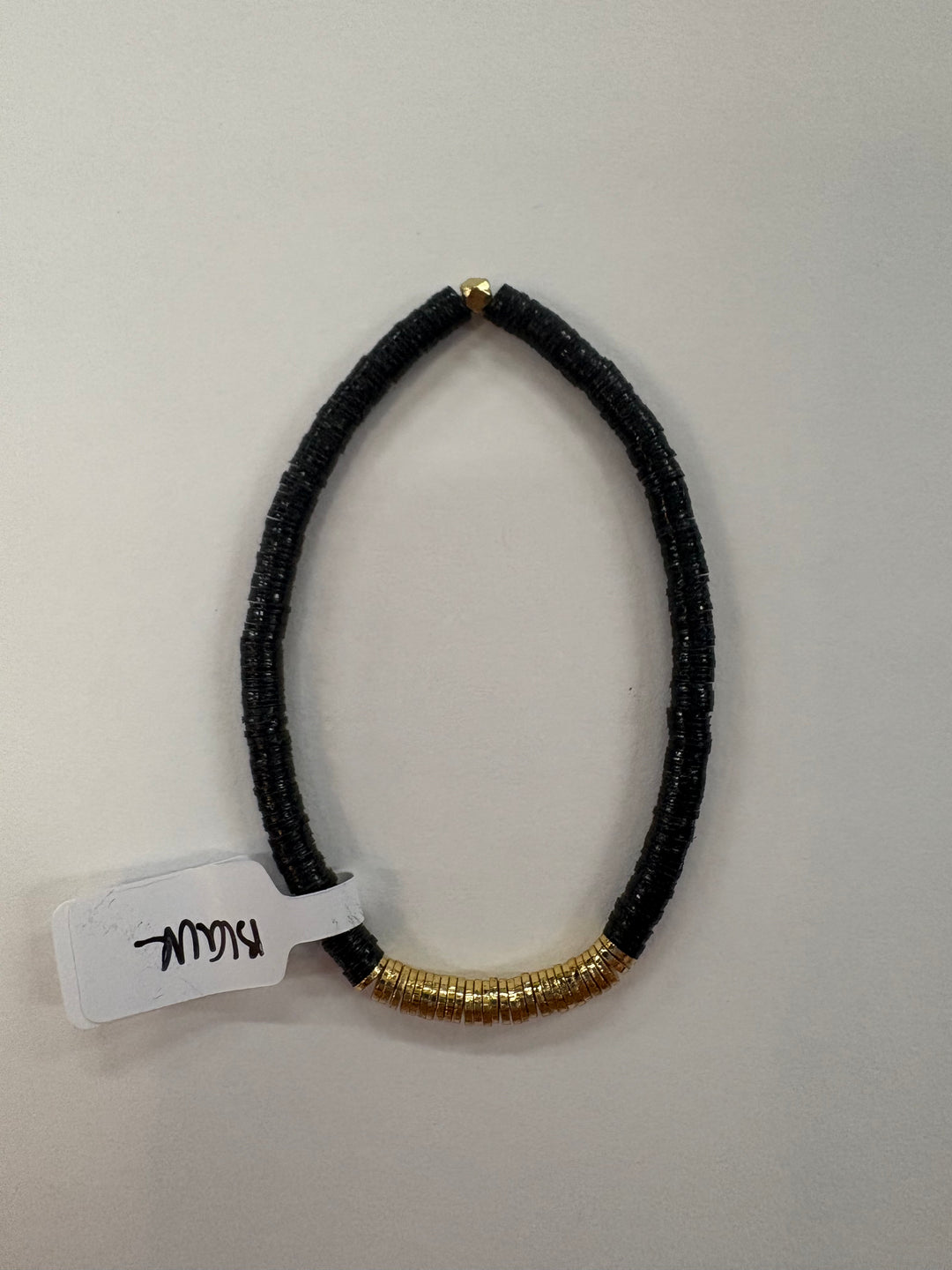 Small flat black bead bracelet with gold-plated beads and a tag that says "Blau."