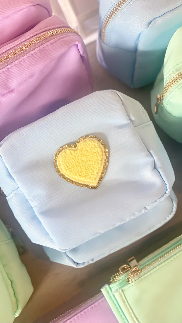 A light blue nylon pouch with a gold zipper and a yellow heart patch.