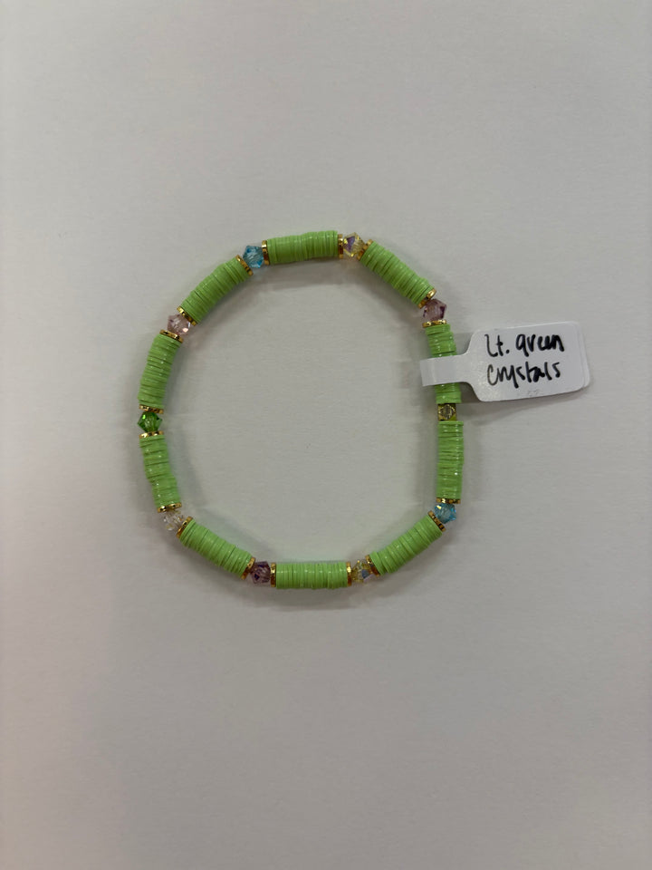A light green flat bead bracelet with colorful crystal accents and a tag reading "Lt. green Crystals."