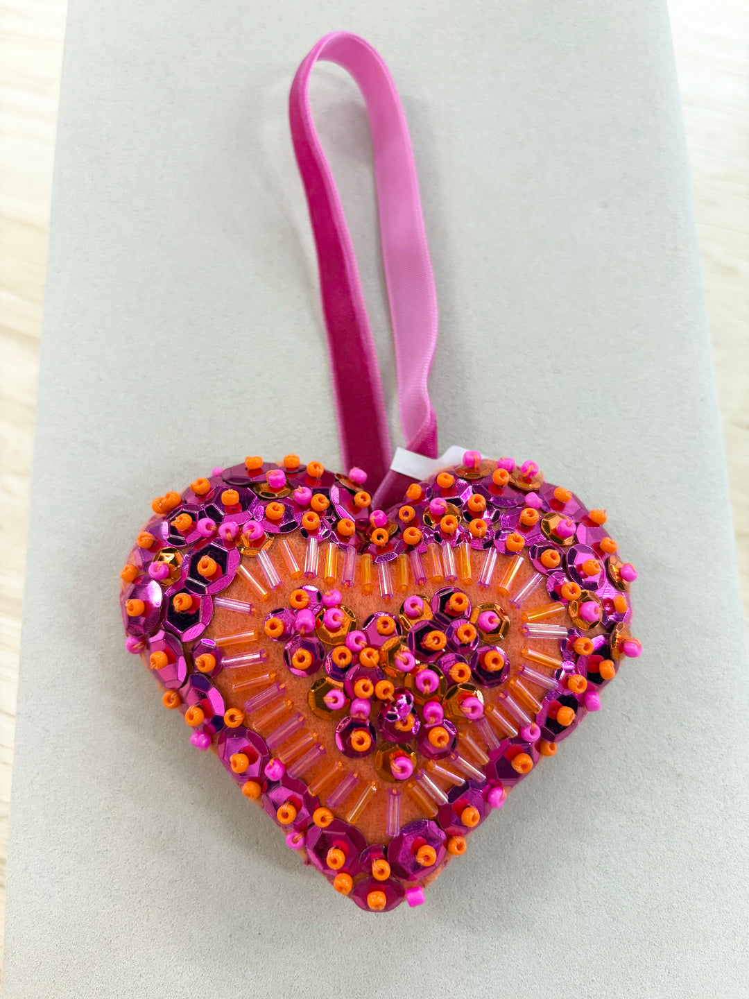 Heart-shaped ornament with pink and orange beads and sequins on an orange fabric.