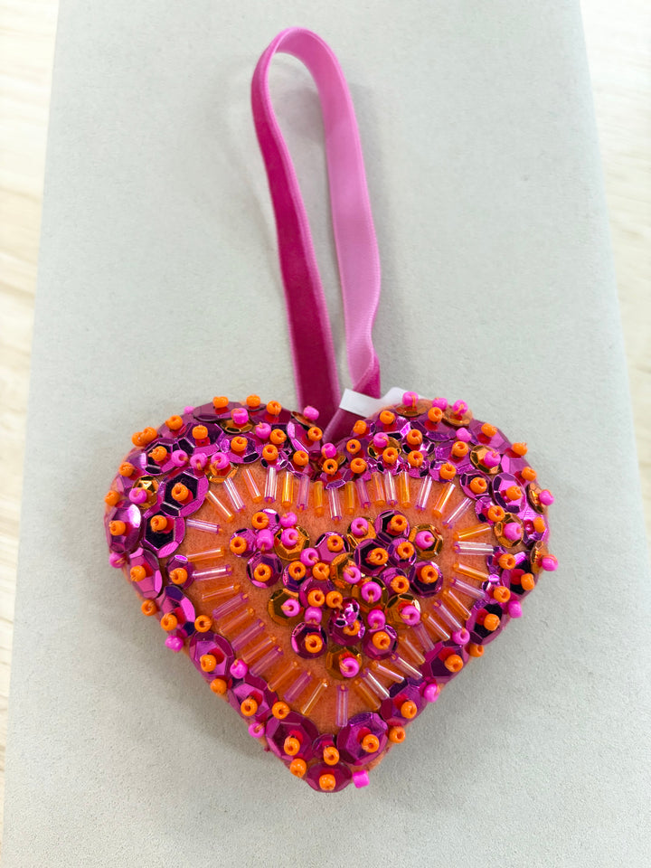 Heart-shaped ornament with pink and orange beads and sequins on an orange fabric.