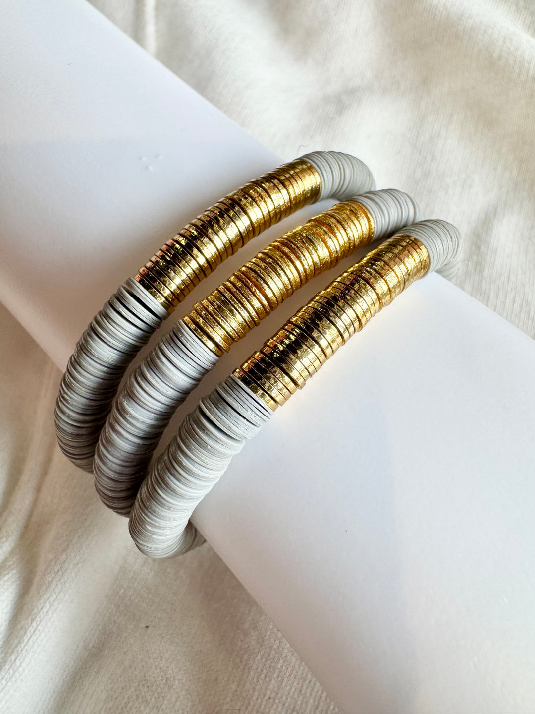 Three large flat bead bracelets with gold and light gray beads are stacked on a white surface.