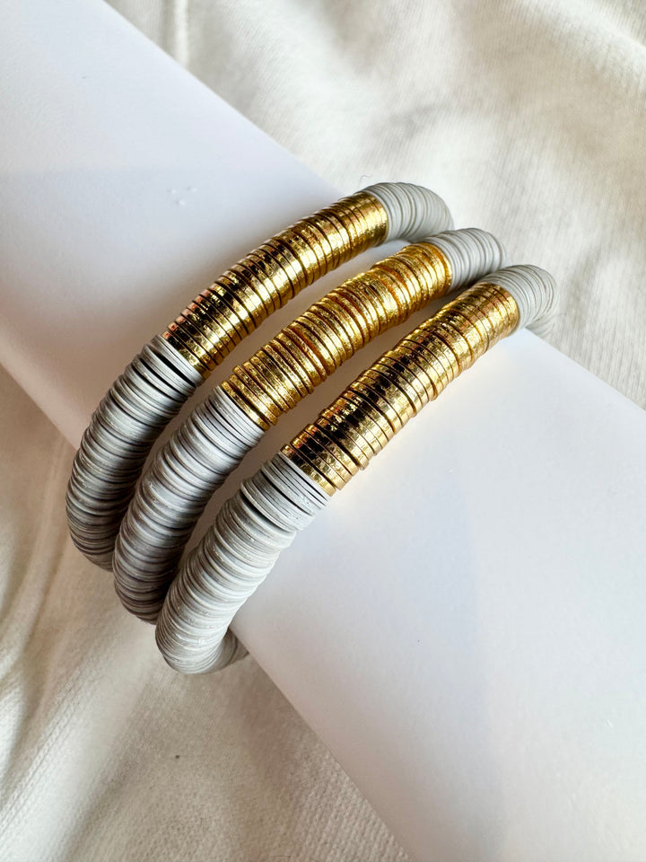 Three large flat bead bracelets with gold and light gray beads are stacked on a white surface.