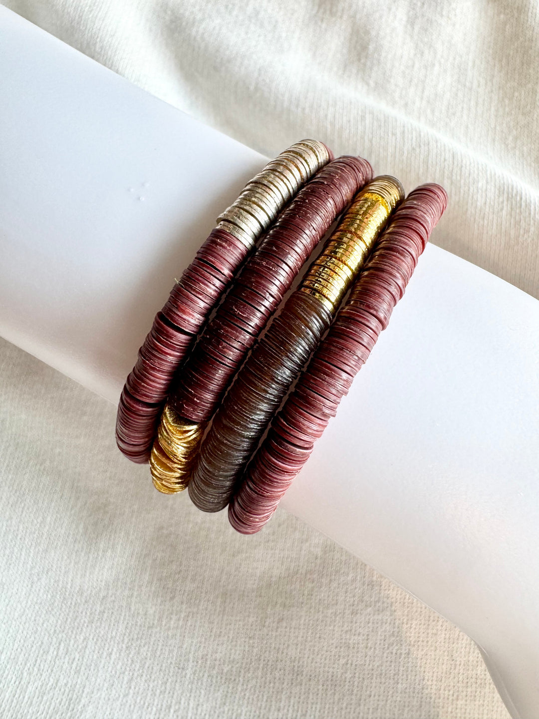 Four stacked bracelets with flat, round vinyl beads in gold, silver, and two shades of maroon.