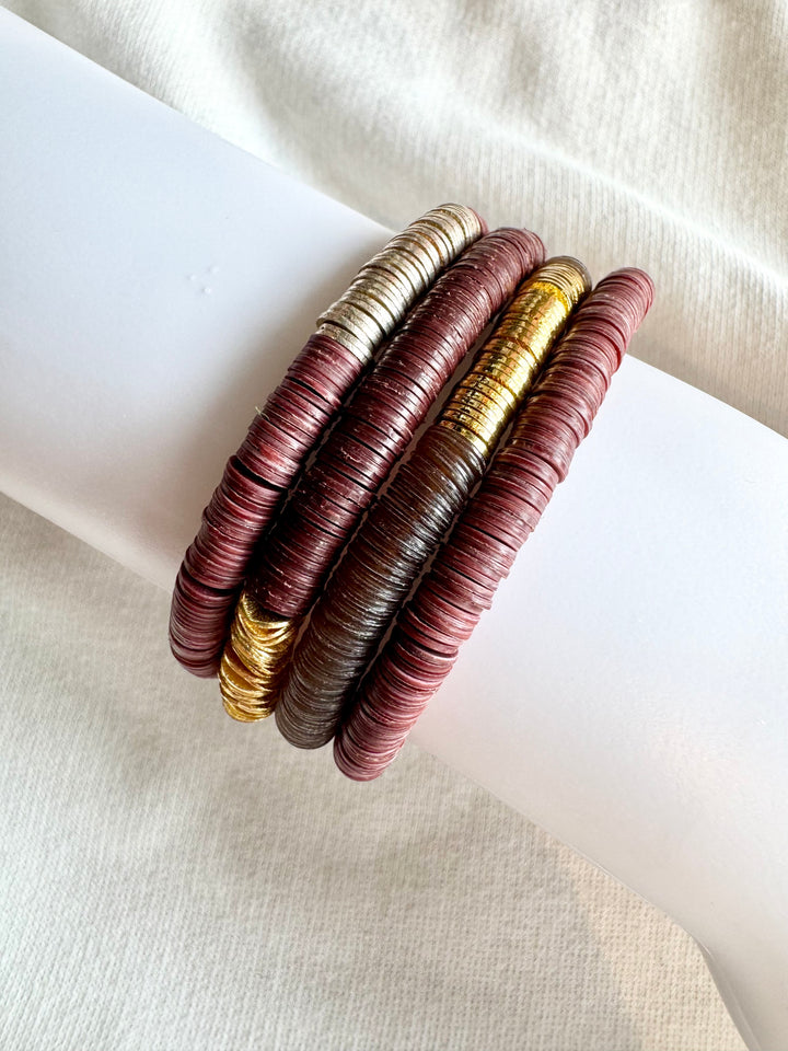 Four stacked bracelets with flat, round vinyl beads in gold, silver, and two shades of maroon.