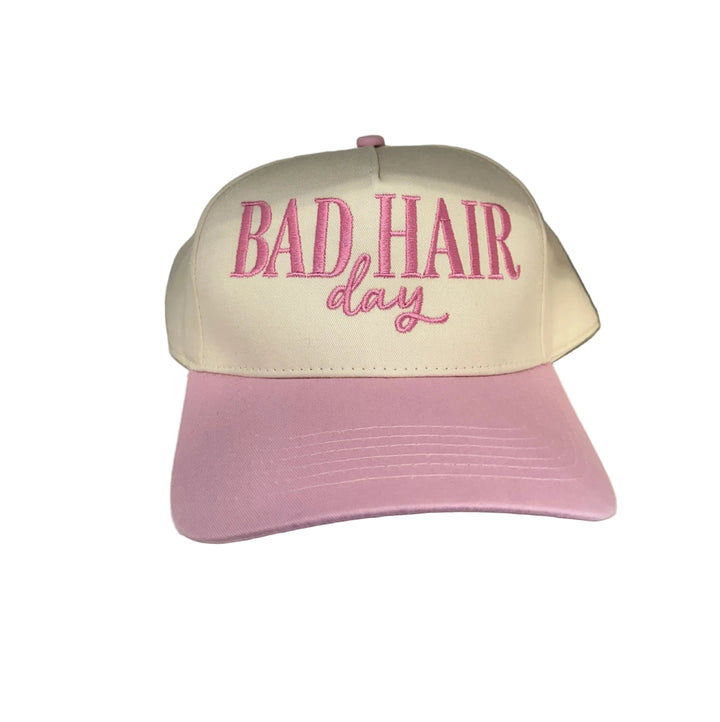 A cream and pink canvas baseball cap with "BAD HAIR day" embroidered in pink.