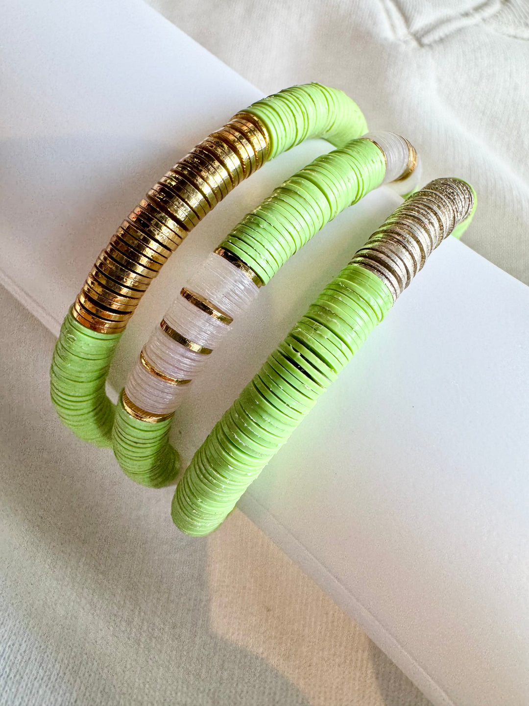 Three flat bead bracelets in light green, white, and gold, with one silver section.
