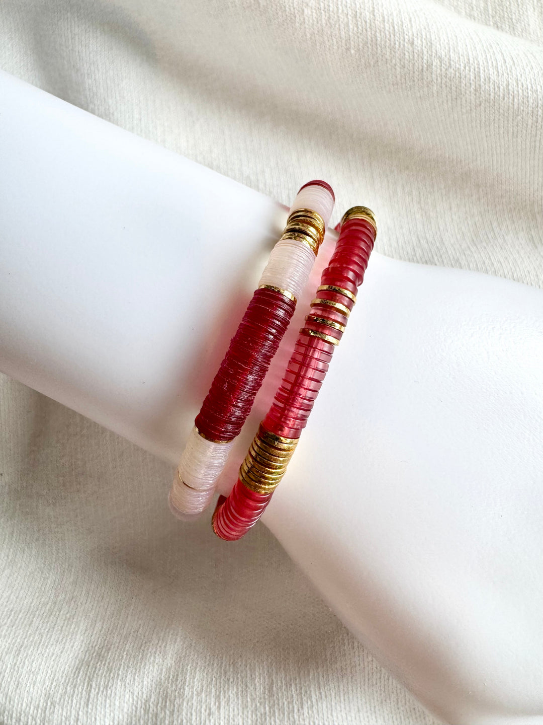 Two red and white flat bead bracelets with gold accents are displayed on a white surface.