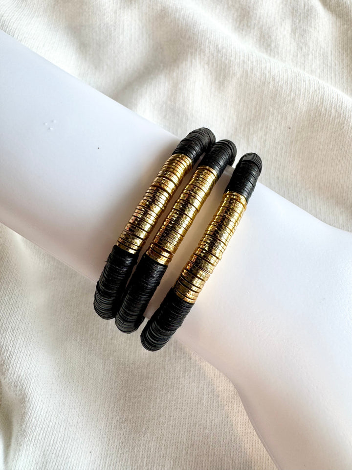 Three black and gold flat bead bracelets on a white surface.