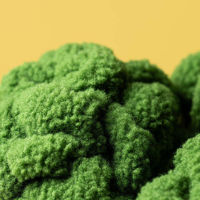 A plush toy broccoli with a textured green crown and a yellow background.