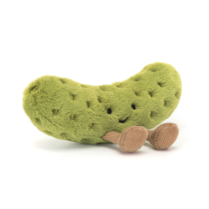 A green plush pickle toy with embroidered eyes and a smiling mouth, sitting on its tan corduroy feet.