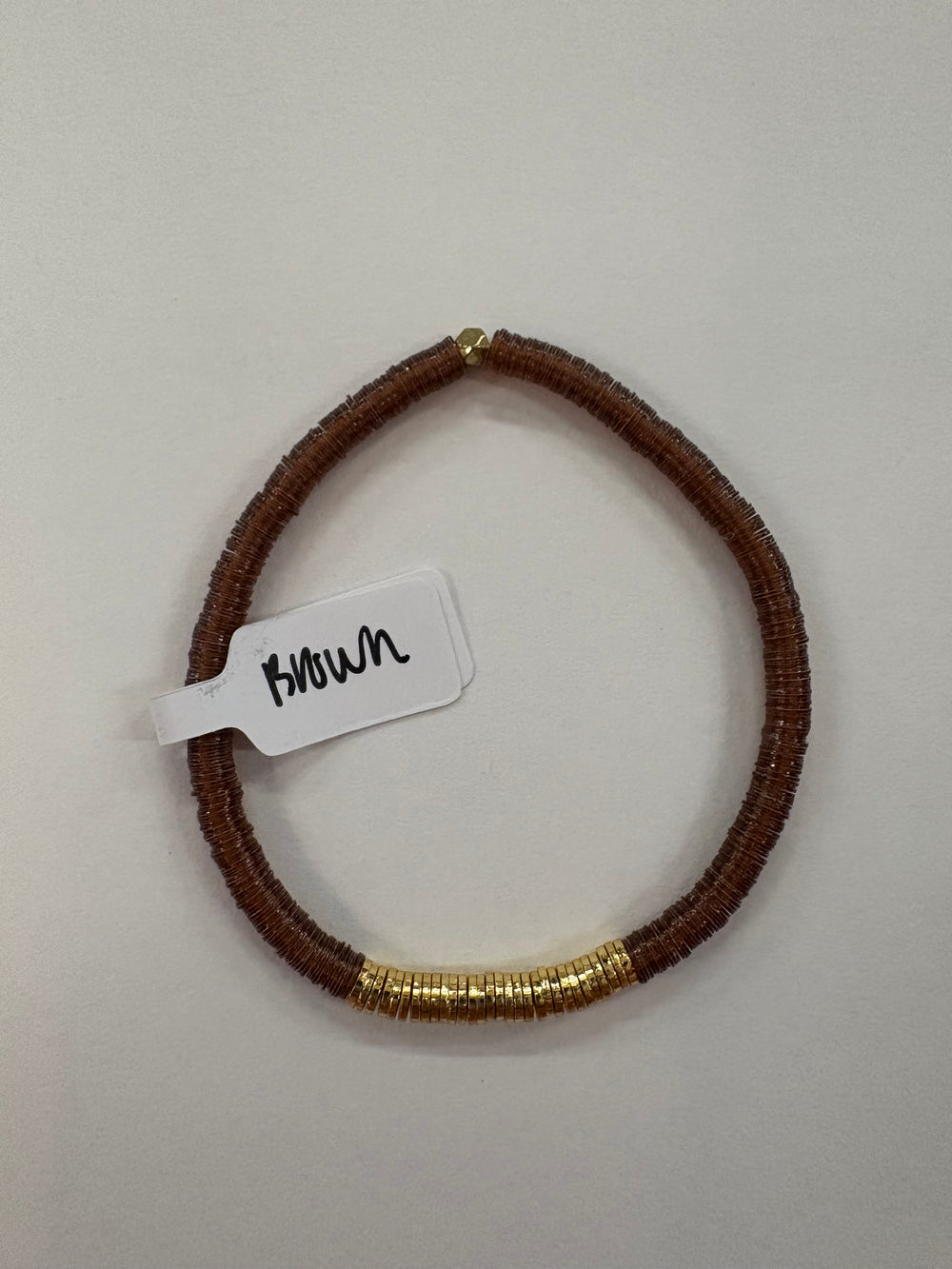 A brown flat bead bracelet with a section of gold-plated beads and a small tag.